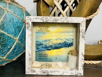 Memorial shadow box with ocean scene, coordinates, and keepsakes.
