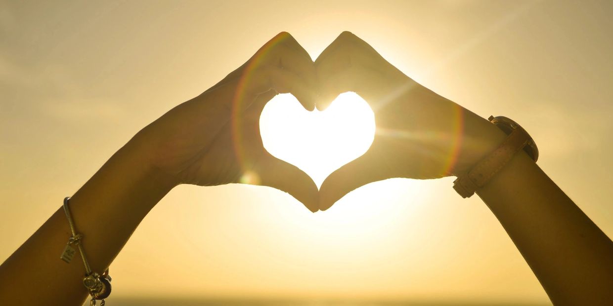 Hands forming a heart shape with sun shining through at sunset.