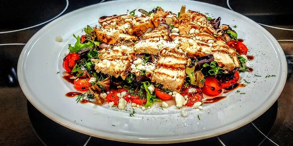 Grilled chicken salad with cherry tomatoes and feta cheese on a white plate.