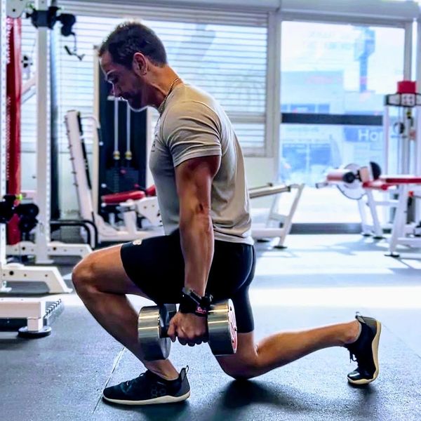 Man performing weighted lunges in a gym.