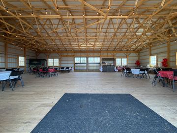 Spacious event hall with wooden floors and tables arranged around the perimeter.