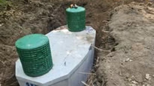 Concrete septic tank with green covers installed in a dug trench.