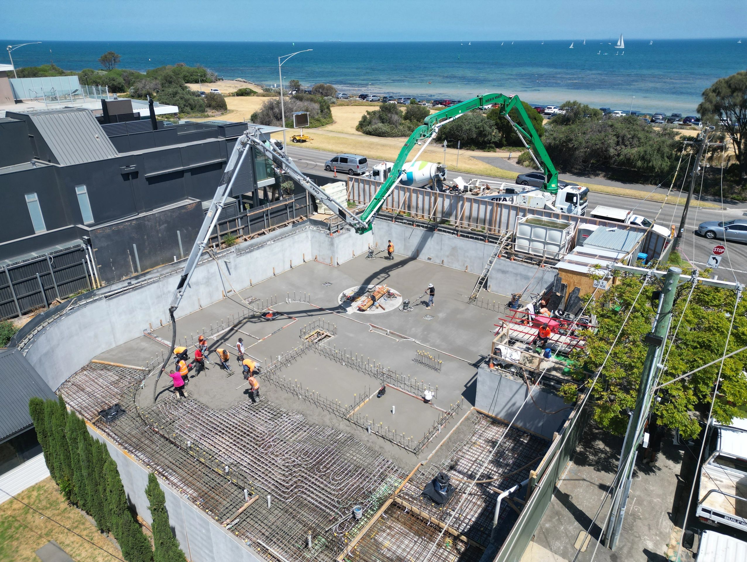 Construction workers pouring concrete near a seaside road with a view of the ocean.
