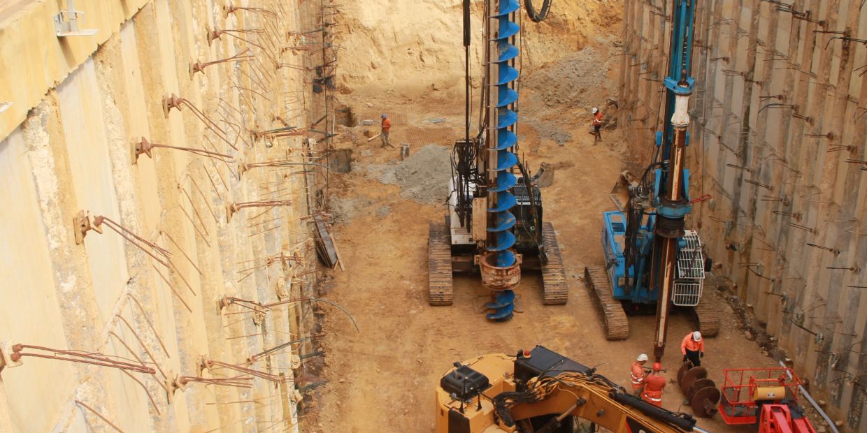 Deep excavation site with drilling machines and workers in safety gear.