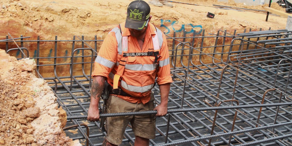 Construction worker handling steel reinforcement bars at a building site.