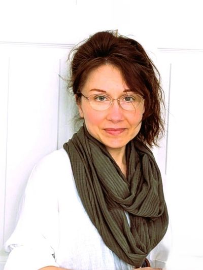Woman with glasses and a brown scarf smiling gently.