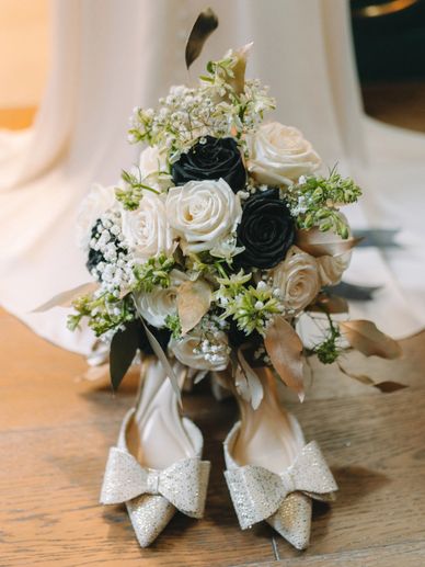 Elegant wedding bouquet with white & black roses, gold foliage & baby’s breath, for a timeless look.