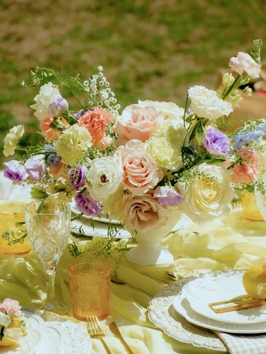 Elegant pastel floral centerpiece with roses  on a yellow picnic table bright outdoor celebration.