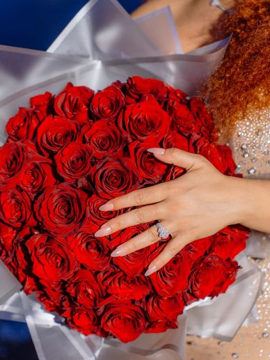 Hand with engagement ring resting on a heart-shaped bouquet of red roses symbolizing love  elegance.