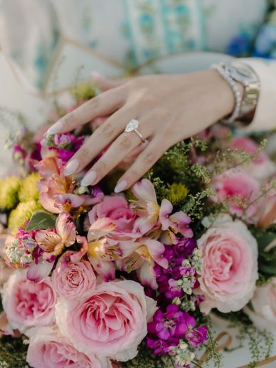 Hand resting on pink floral bouquet with roses and alstroemeria, elegant engagement or celebration.