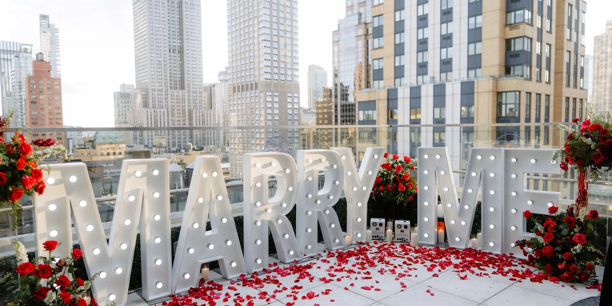 Romantic illuminated “Marry Me” sign surrounded by candles and florals, perfect for proposal setups!