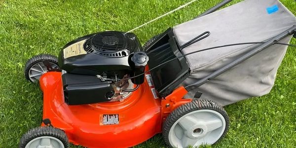Orange and black lawn mower on green grass.