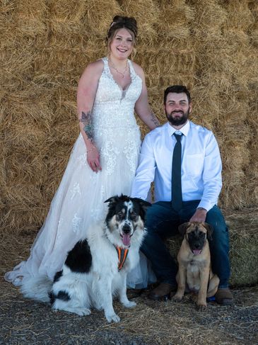 Bride and groom with two dogs in front of hay bales.