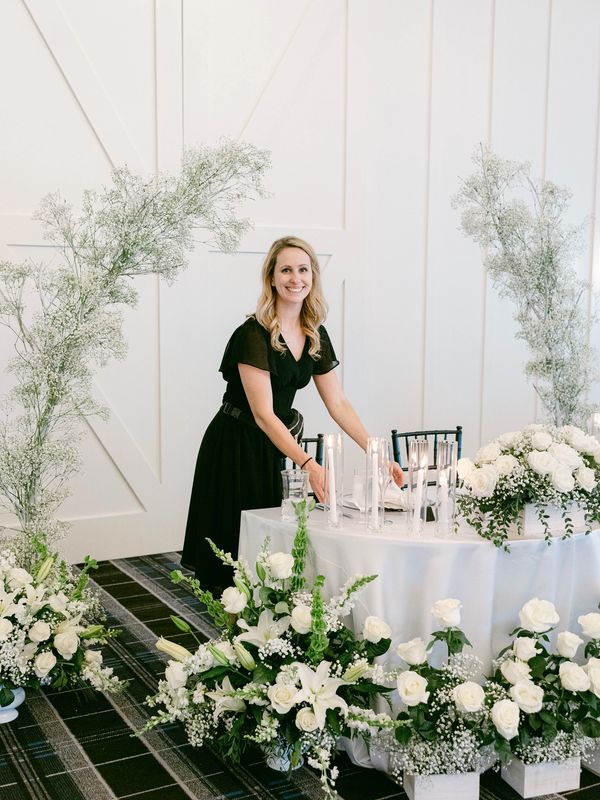 A woman in black arranging a floral-decorated table with candles.