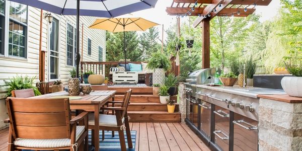 Cozy outdoor patio with wooden furniture, umbrellas, and a stainless steel grill station.