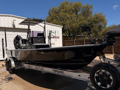Black fishing boat on a trailer in a driveway under clear skies.
