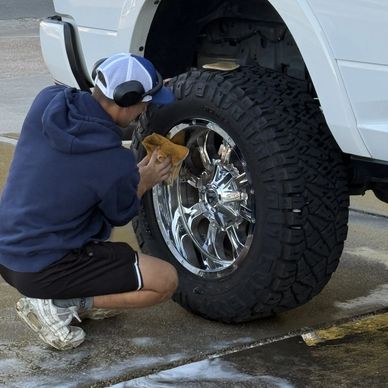 Guy is cleaning a Dodge Cummins and shining the chrome wheel on it.