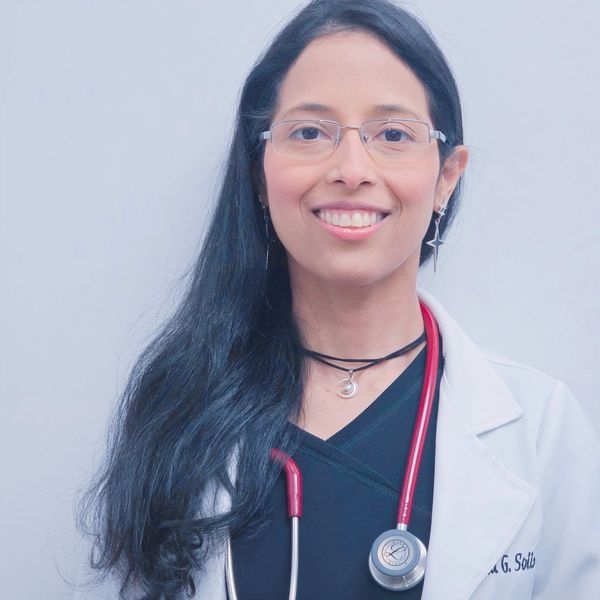 Smiling female doctor with long hair and glasses wearing a white coat and stethoscope.