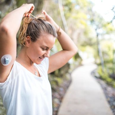 A woman with a glucose monitor on her arm outdoors on a walking path.
