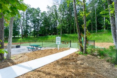 A fenced dog park with a picnic table and green surroundings.
