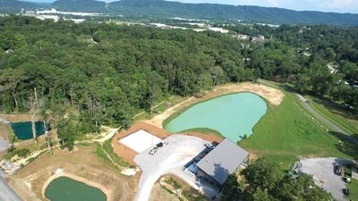 Aerial view of a small pond and building surrounded by greenery and hills.