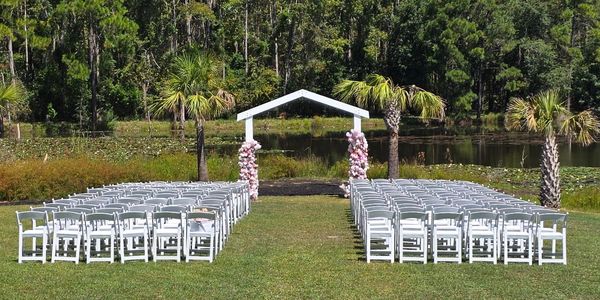 Outdoor wedding setup with white chairs and a decorated arch.