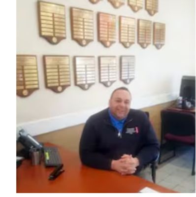 Man sitting at a desk in an office with plaques on the wall.