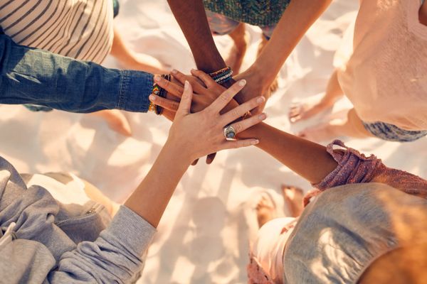 Diverse group joining hands in unity on a sandy beach.