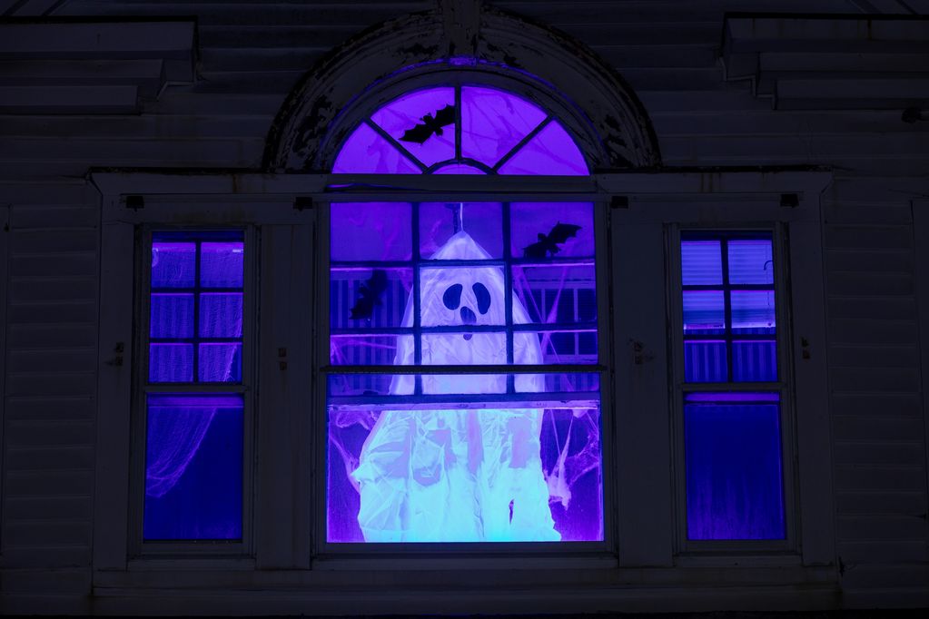 Ghost decoration in a purple-lit window with bat cutouts.