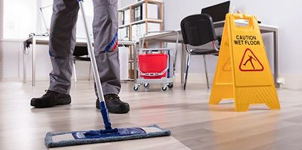 Person mopping a clean office floor with caution sign nearby.