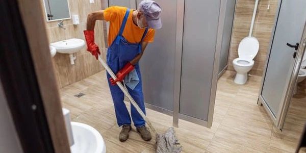 Janitor mopping the floor in a public restroom wearing protective gloves.