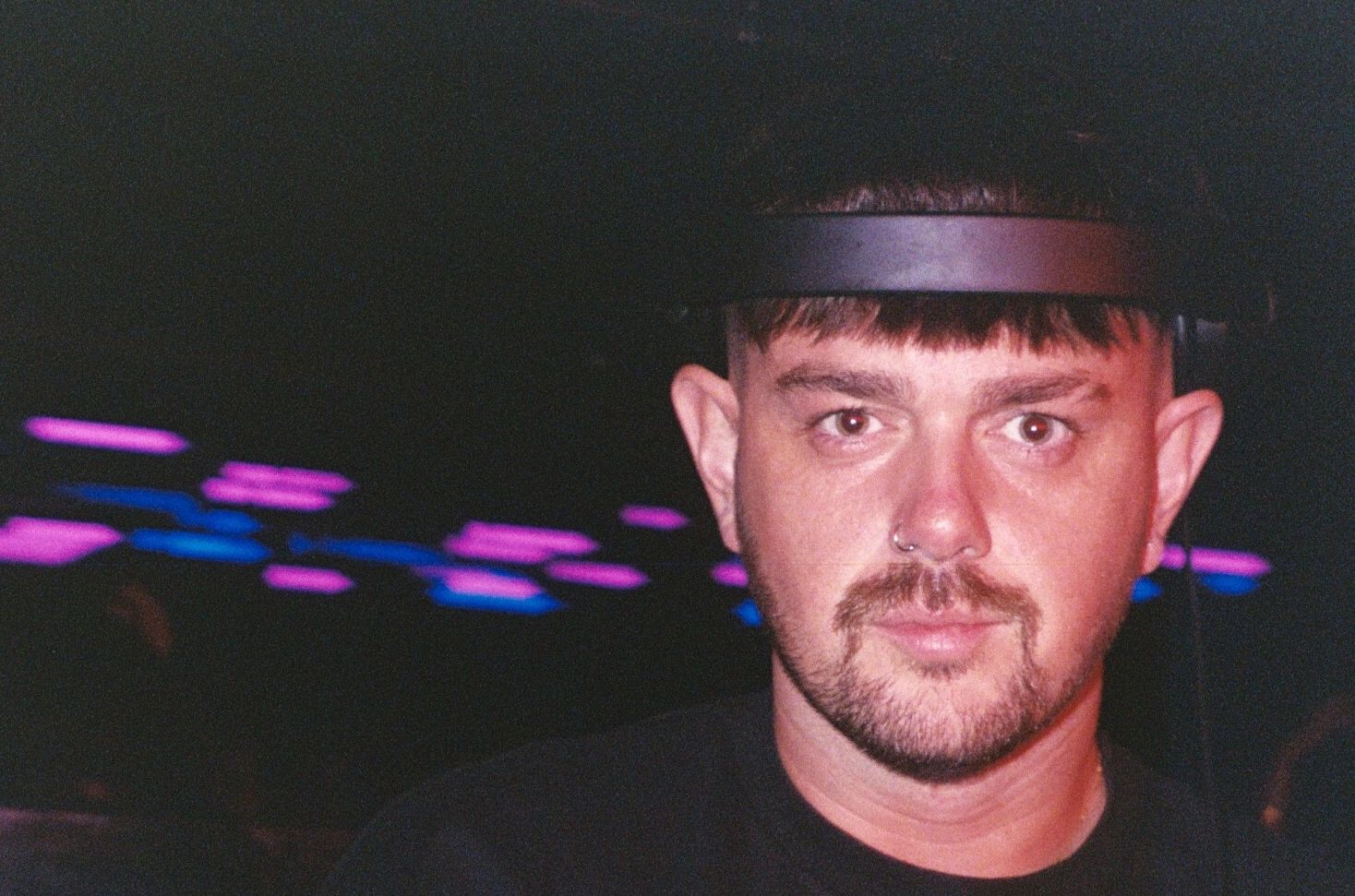 Man wearing headphones in a dimly lit club with colorful lights.