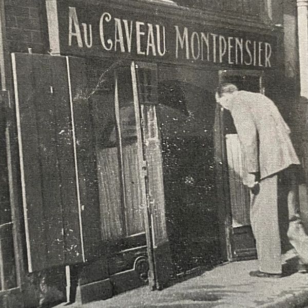A man peeks into a small entrance under a sign Au Caveau Montpensier