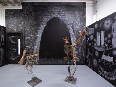 Art installation with skeletal metal sculptures and black-and-white mural.