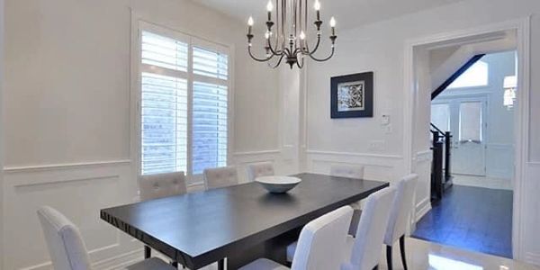 Bright dining room with a wooden table and white cushioned chairs under a chandelier.