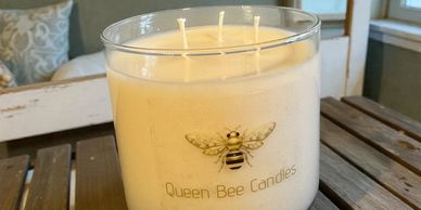 A large Queen Bee Candles jar candle with three wicks on a wooden surface.