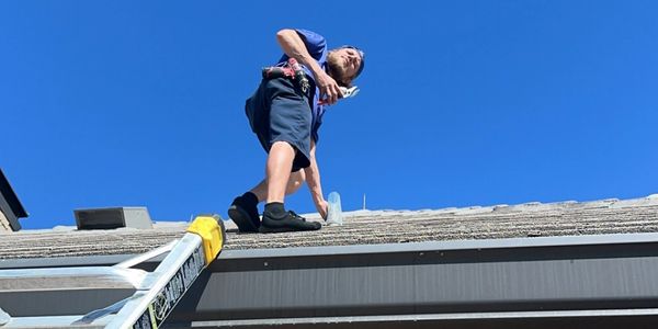 Man working on a roof under a clear blue sky with a ladder.