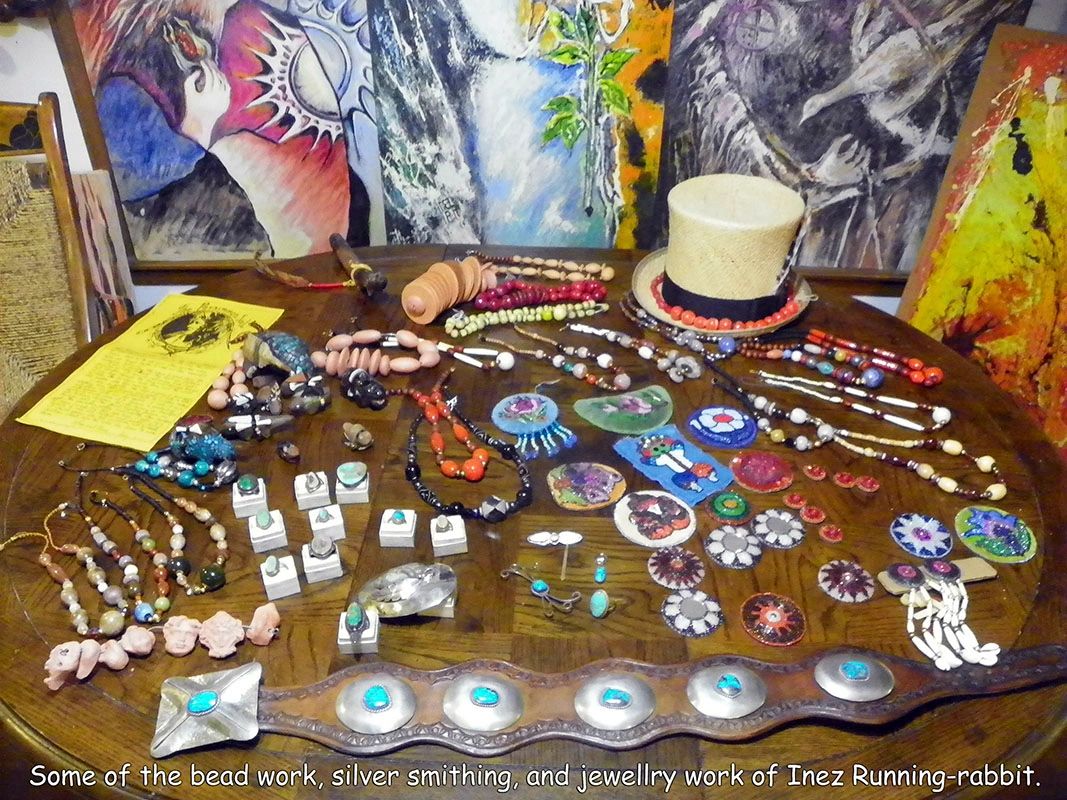 A photo of Inez Running-rabbit's jewelry, and some of her paintiings behind the table.