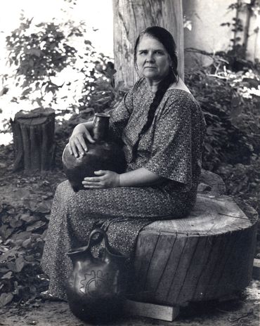 Inez Running-rabbit sitting on a tree stump holding one of her pots.