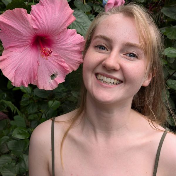 Smiling garden designer georgina morris posing next to a large pink hibiscus flower outdoors.