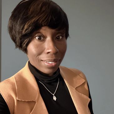 Woman with short hair, wearing a tan vest and black turtleneck, smiling gently.