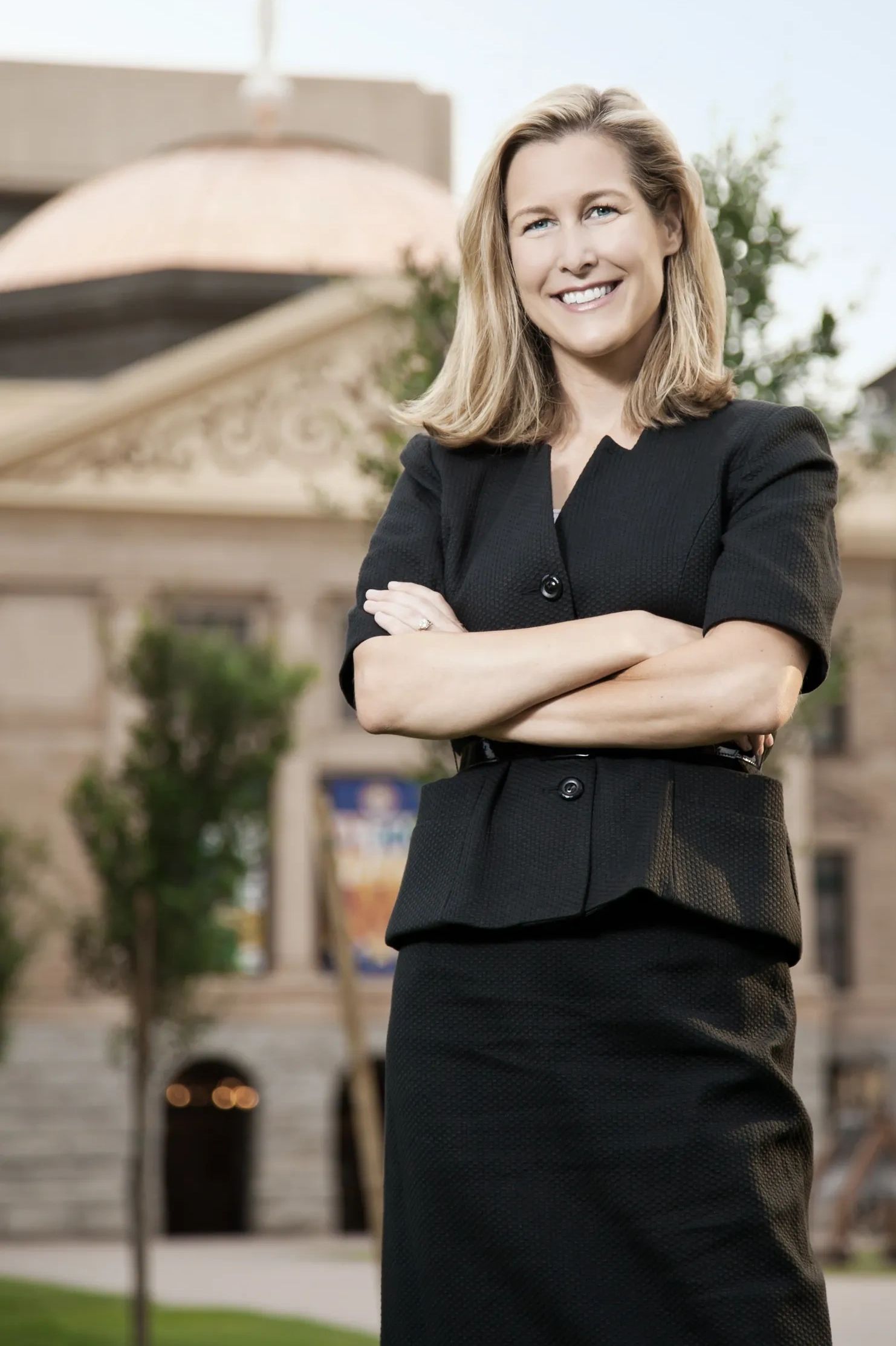 Gretchen Jacobs standing in front of the Arizona Capitol, smiling with her arms crossed.