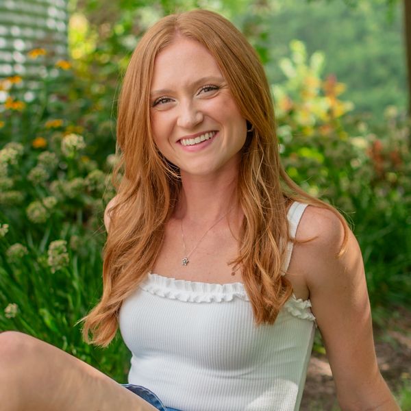 Young red-haired woman smiling outdoors in a garden.