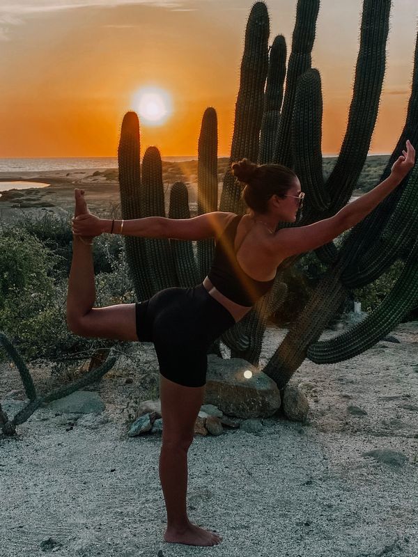 Woman practicing yoga at sunset near tall cacti in a desert landscape.