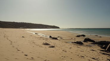 A serene beach with footprints and rocks under a clear sky.