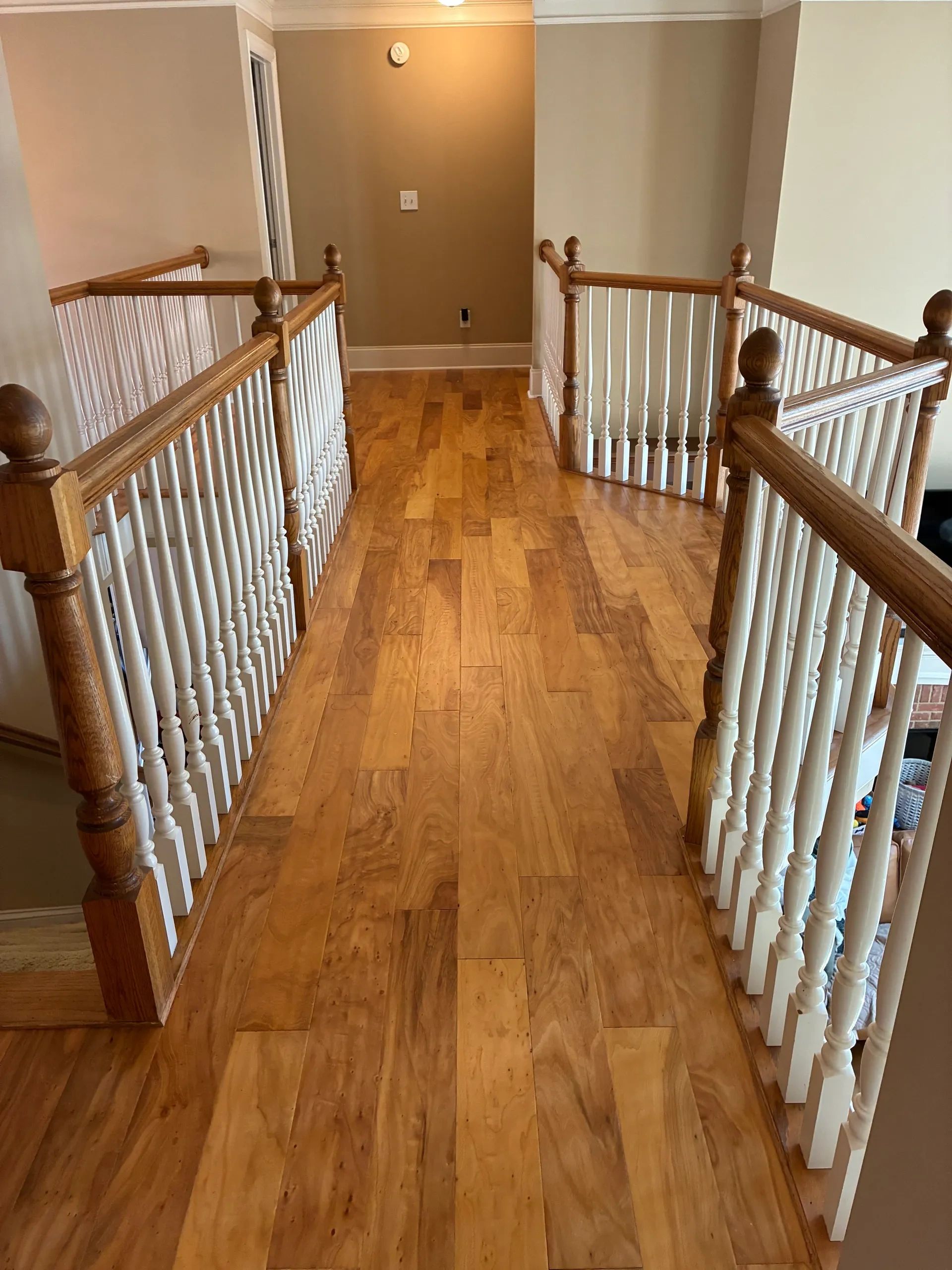 Wooden staircase railing with white balusters on a hardwood floor.