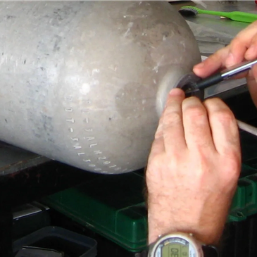 Hands inspecting or working on a metal cylinder.