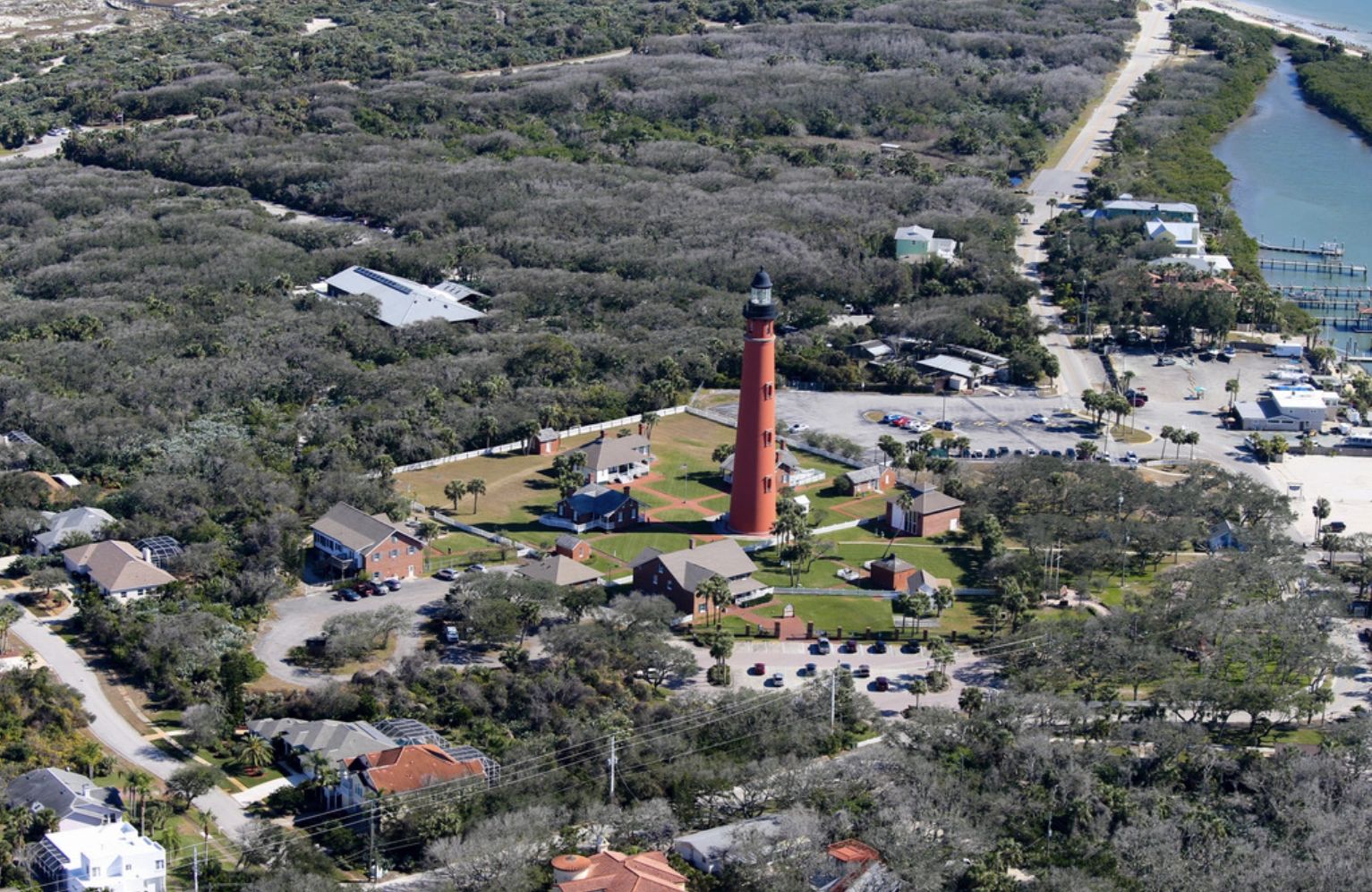 Aerial view of a lighthouse surrounded by buildings and greenery.
