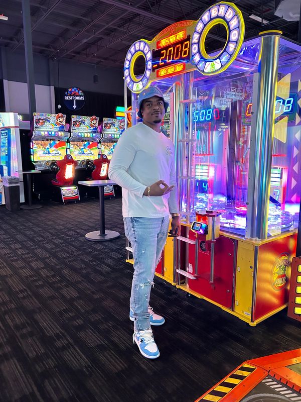 A man poses beside a brightly lit arcade game in a vibrant gaming center.