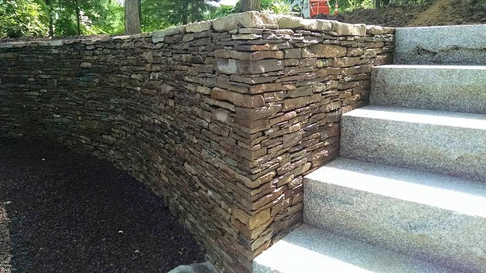 Curved stone retaining wall next to granite stairs in a garden